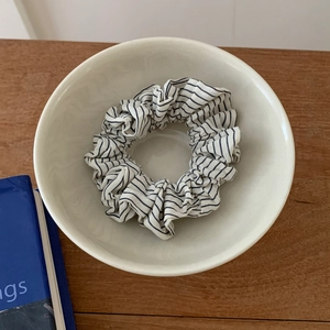 Close-up of a black and white striped fabric scrunchie in a white ceramic bowl on wood