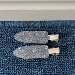 Detail of two silver metal hair clips with grey sparkling crystals on a blue background
