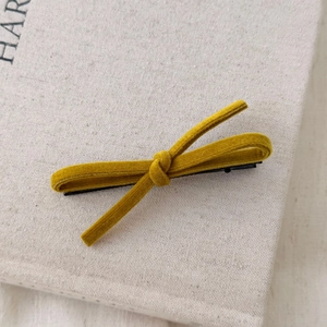 Detail of a ginger yellow velvet bow hair clip with a black metal duckbill base
