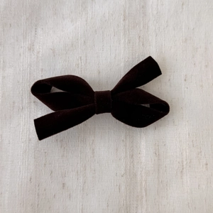 Detail of elegant dark brown velvet bow hair clip on a textured fabric background