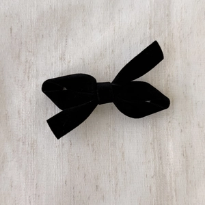 Detailed top view of a black velvet bow hair clip on a beige linen fabric background