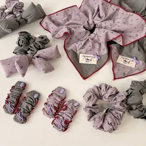Floral gray and purple fabric scrunchies and bow hair ties set on white surface