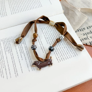 Detailed macro shot of dachshund charm and textured beads on brown ribbon scarf jewelry
