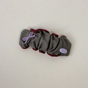 Detail showing grey pleated fabric hair scrunchie with red trim and purple resin bow