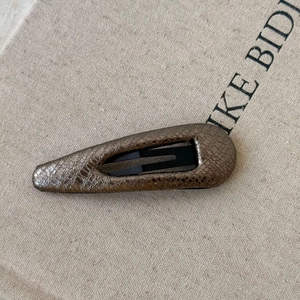 Macro view of geometric water-drop hair clip with bronze snake skin pattern texture