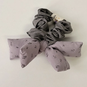 Detail of puffy floral bow hair tie featuring grey pleated band and purple fabric textures