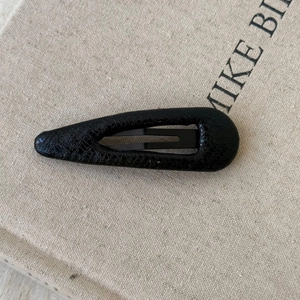 Detailed macro view of black faux leather textured drop-shaped BB hair clip on fabric