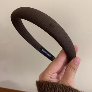 Close-up of brown textured fabric headband featuring a stitched handmade label detail