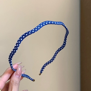 Détail d'un serre-tête fin bleu marine à pois avec des embouts en métal doré