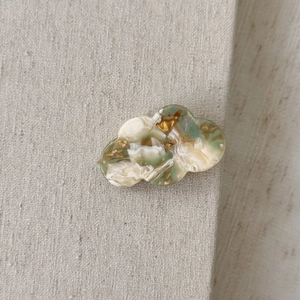 Detail view of cloud-shaped acetate hair clip with green marble texture and gold lettering
