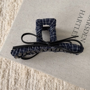 Close-up of navy plaid hair claw clip with black leather bow on a soft fabric base