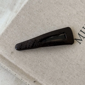 Detail of dark brown faux leather hair clip with texture on linen book cover