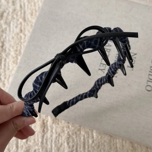 Close-up of blue plaid headband with black leather bow and punk style spikes