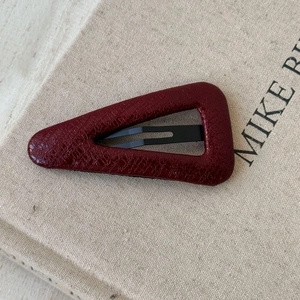 Detail of dark red faux leather hair clip with crocodile texture on a beige background