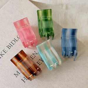 Five gradient acetate hair claws set in pink, green, and marble patterns on a book