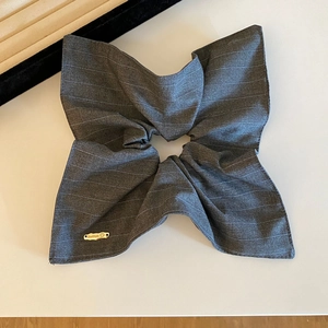 Grey striped fabric bow hair accessory with handmade metal logo on beige background