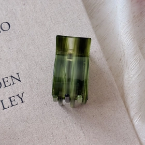 Close-up of small green striped acetate hair claw clip on a textured fabric background