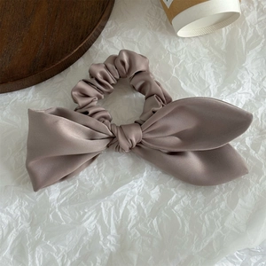 Elegant champagne satin scrunchie with asymmetrical bow on a wooden surface