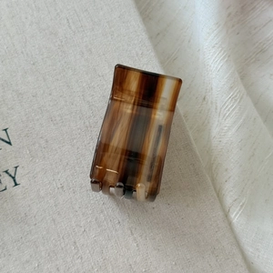 Detail of a rectangular tortoiseshell acetate hair claw clip on cream fabric background