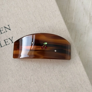 Detail of tortoise shell acetate hair clip with cherry rhinestone design on fabric background