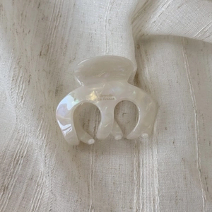 Detail of a creamy white acetate hair claw clip with pearlescent finish and gold lettering