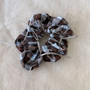 Close-up of a plaid scrunchie with delicate silver-grey ribbon bows on soft linen cloth