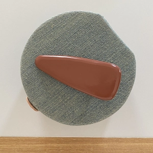 Glossy caramel brown teardrop hair clip with polished finish on denim texture base