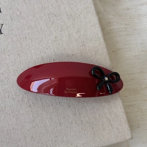Close-up of a burgundy acetate oval hair barrette with a black bow and crystal accent