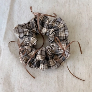 Close-up of ballet-style plaid scrunchie with brown ribbons on linen background