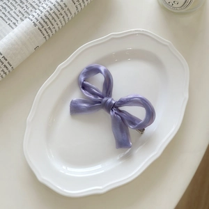 Elegant purple satin bow hair clip with glossy finish on a white decorative plate