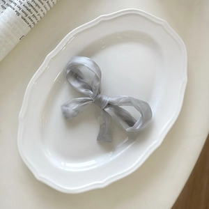 Close-up of elegant silver-grey organza bow hair clip on a decorative white porcelain plate