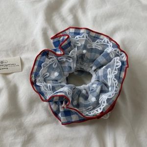 Détail d'un chouchou à carreaux bleu marine avec dentelle blanche et bords rouges