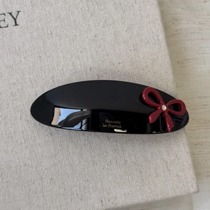 Close-up of a black oval acetate hair clip with a red bow and gold French engraving