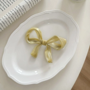 Detailed texture of a silky pale gold ribbon bow hair clip on a vintage ceramic plate