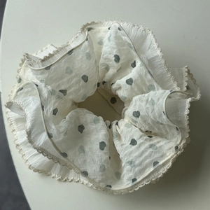 Dettaglio di scrunchie in chiffon beige con cuori verdi e bordi in pizzo raffinato