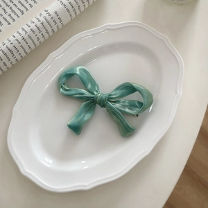 Detail view of a mint green glossy ribbon bow hair clip on a vintage porcelain plate