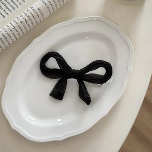 Detail view of a black translucent fabric bow hair clip on a vintage white ceramic plate