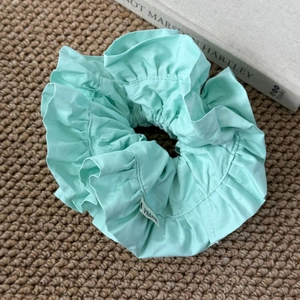 Détail d'un chouchou plissé vert menthe sur un tapis tissé avec une esthétique douce