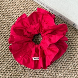 Détail d'un chouchou rouge à volants avec étiquette FMdre sur texture tissée