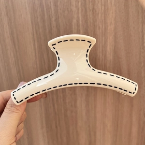 Cream large claw clip with black hand-painted dotted edges on a vertical wooden background