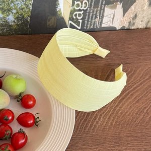 Detail of yellow wide headband featuring micro-grid fabric texture on a wooden desk