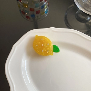 Close-up of a lemon-shaped acetate hair clip with sparkling rhinestones on a white plate