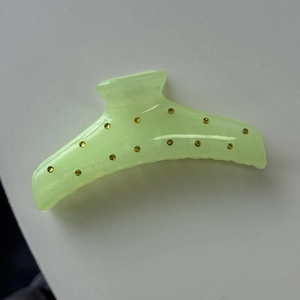 Close-up of translucent neon green hair claw clip with sparkling golden rhinestones