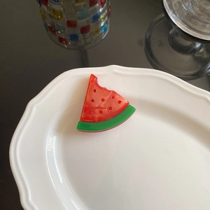 Detail view of acetate watermelon hair clip with red rhinestones on a decorative plate