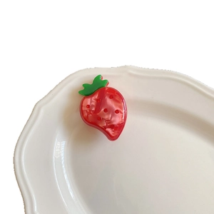 Cute strawberry acetate hair clip with sparkling red rhinestones on a ceramic dish
