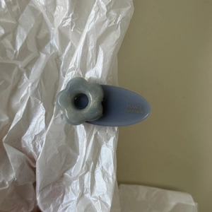 Détail d'une pince à cheveux ovale bleu mat avec fleur en résine et marquage doré