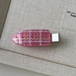 Detailed view of a pink checkered hair clip with gold glitter on beige linen background