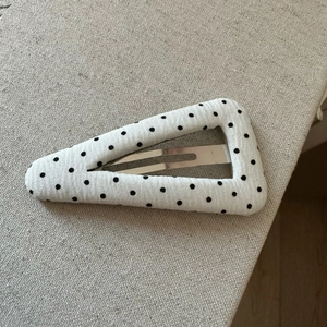 Détail d'une pince à cheveux en tissu blanc à pois noirs sur clip métallique BB