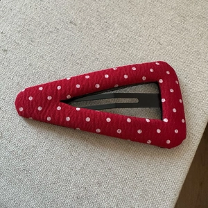 Détail d'une pince à cheveux triangulaire en tissu rouge à pois sur fond de lin texturé
