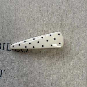 Macro detail of a cream-colored hair clip with black polka dots on linen fabric